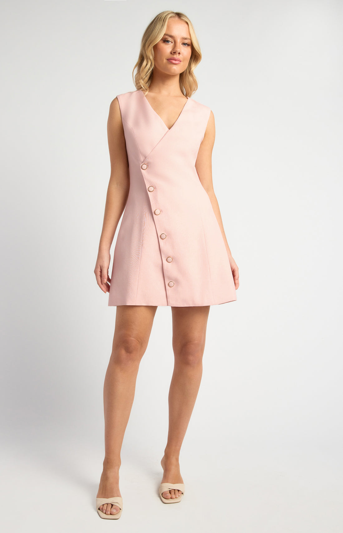 Model wearing blush pink asymmetrical button vest mini dress